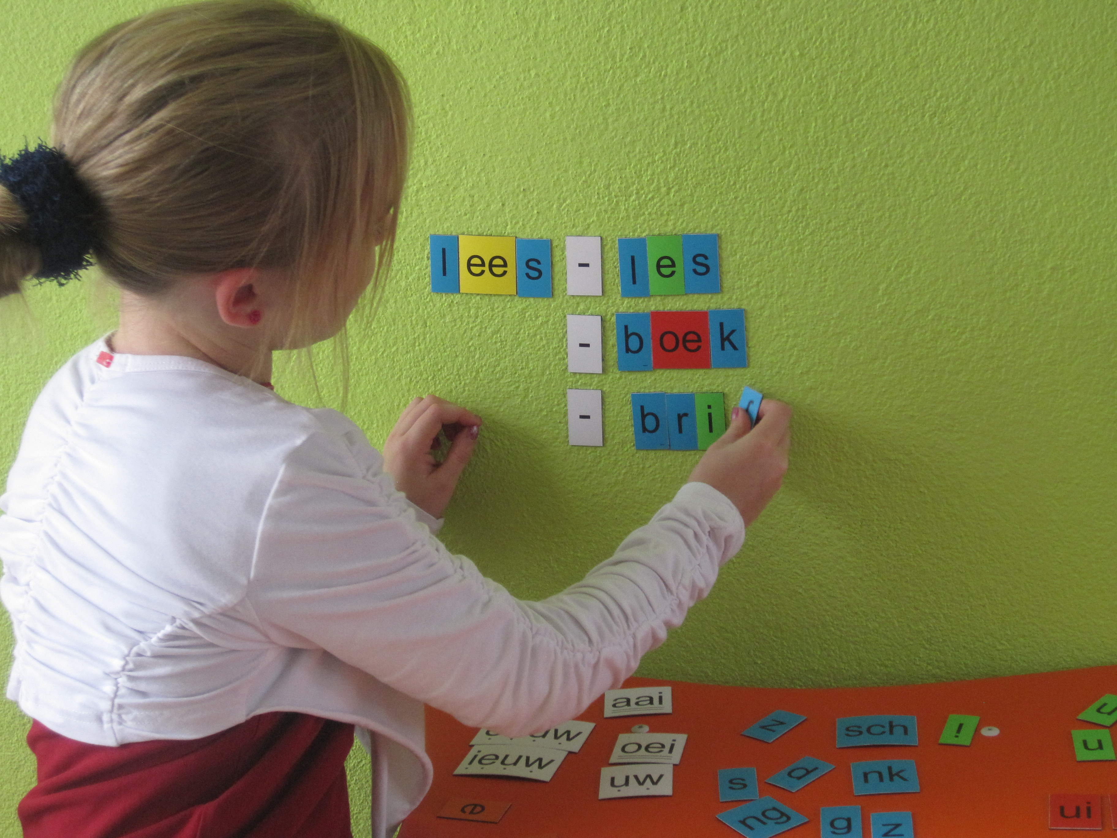 Een meisje plakt gekleurde letters op een magneetbord